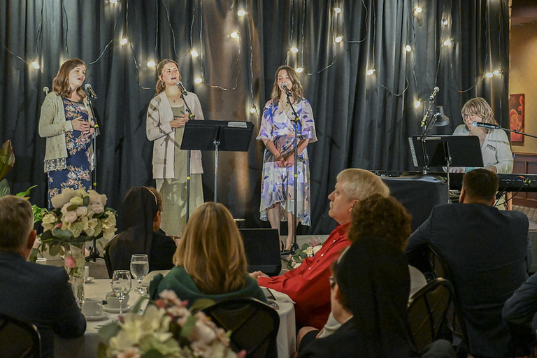 three women singing a song with a keyboard accompanyist