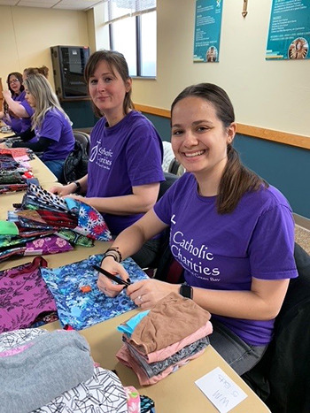 women in a row wearing purple Catholic Charities tshirts while working with fabric