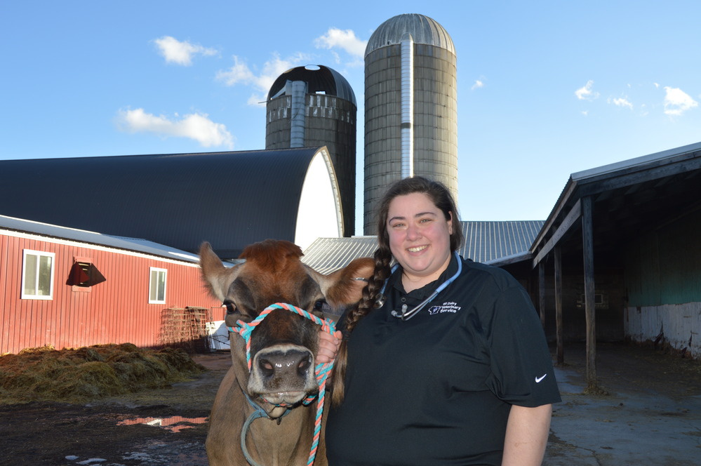 Abby Michels smiling and standing next to a cow with a barn and silos in the background