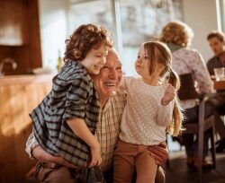 Smiling grandfather hugging grandchildren at home kitchen