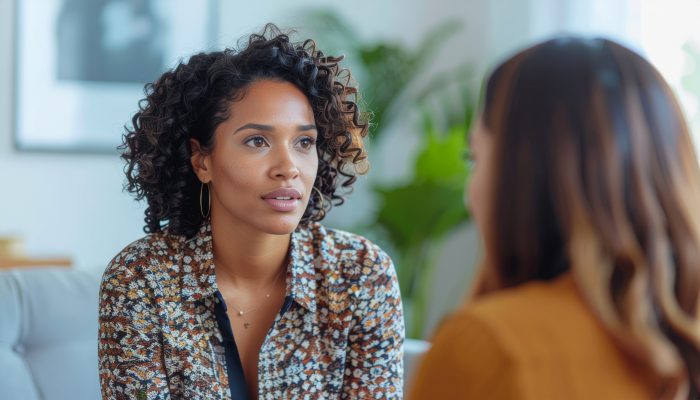Two women engaged in serious conversation. One woman has curly hair. The other woman is facing away from the camera.
