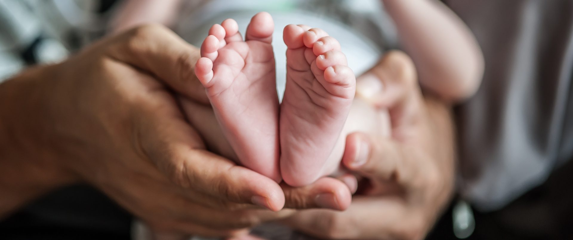 Close-up detail of parent holding cute and soft baby small leg in his hands.