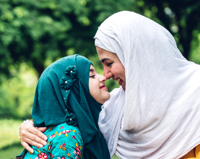 Portrait of happy lovely family arabic muslim mother and little muslim girls child with hijab dress smiling and having fun hugging and kissing together in summer park