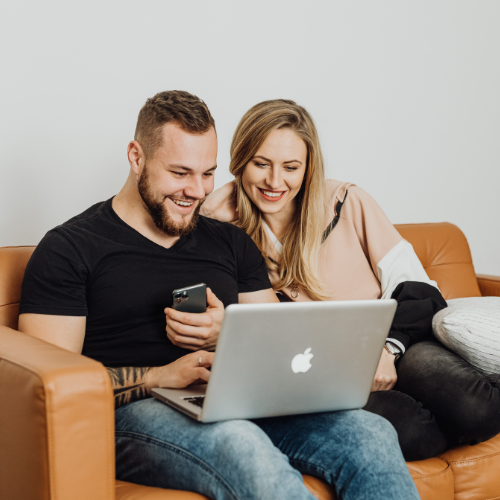 couple sitting on couch looking at laptop