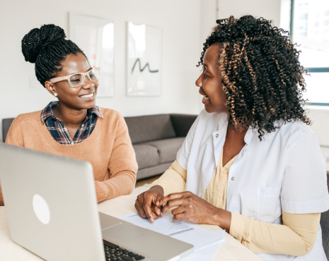 two women sitting down with a computer in front of them