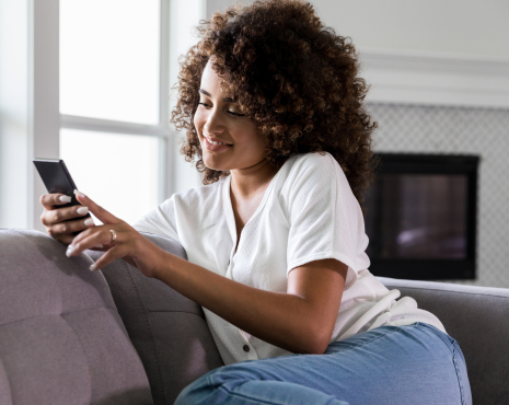 Woman In Living Room Sitting On Couch Smiling At Phone
